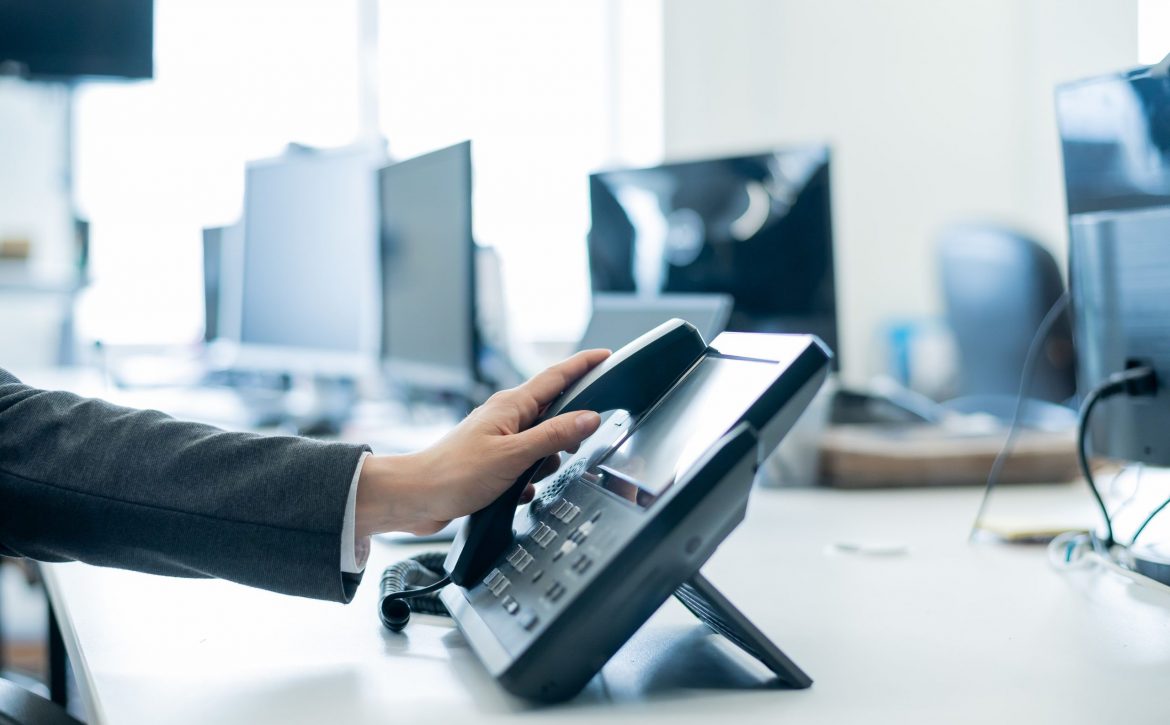 Close-up of a female employee's hand on a landline phone. Woman picks up a push-button telephone at the workplace in the office