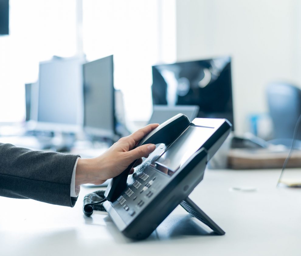 Close-up of a female employee's hand on a landline phone. Woman picks up a push-button telephone at the workplace in the office